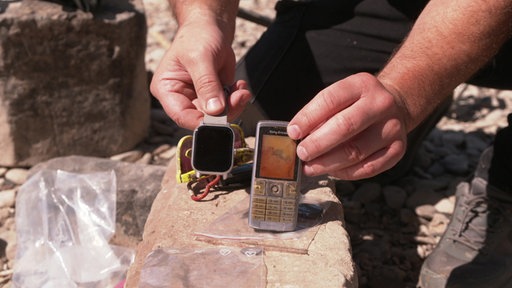 Eine Person hält ein altes Handy und eine Smart-Watch in die Kamera