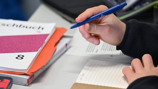 Ein Schüler schreibt mit einem Kugelschreiber in ein Heft