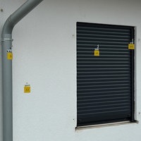 Mit gelben Polizeimarkierungen versehene Einschusslöcher an einer Wohnhaus-Wand mit einem Fenster, das mit einem Rollladen verschlossen ist