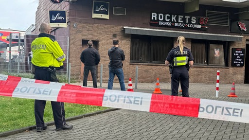 In einem abgesperrten Bereich vor einer Bar in Köln stehen mehrere Einsatzkräfte der Polizei