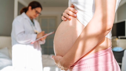 Schwangere Frau hält ihren Bauch bei Arztuntersuchung