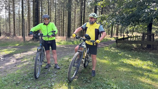 Dieter Rowek (re.) und Winfried Dreisbach sind mit ihren Fahrrädern im Wald.
