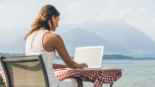 Eine Frau sitzt mit Laptop am Wasser