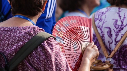 Eine Frau wedelt sich bei heißem Sommerwetter mit einem Fächer Luft zu