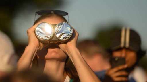 Mehrere Personen schauen sich die Sonnenfinsternis an. Eine Person hält ein spezielles Fernglas.