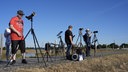 Drei Personen stehen mit Kameras und Stativen bereit für die Sonnenfinsternis