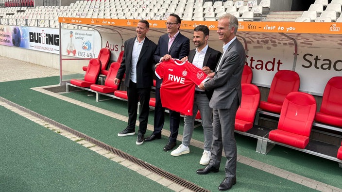 Marc-Nicolai Pfeifer (Vorstandsvorsitzender Rot-Weiss Essen), Markus Krebber (Vorstandsvorsitzender RWE), Alexander Rang (Vertriebschef Rot-Weiss Essen) und Michael Marhofer (Geschäftsführer ifm) halten ein rotes Trikot mit der Aufschrift "RWE"