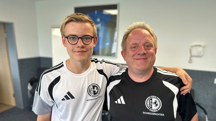 Ein Sohn hält seinen Vater im Arm. Beide tragen Sporttrikots.