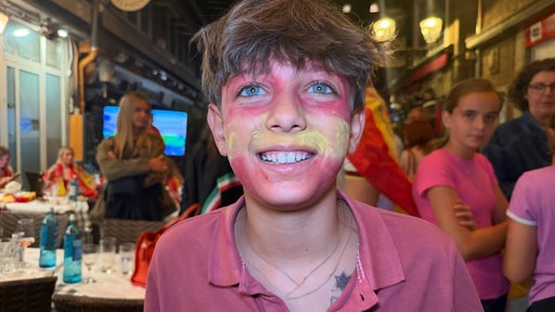 Ein Junge, Alex, hat mit Farbe die spanische Flagge auf das Gesicht gemalt