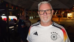 Ein Mann im Deutschland-WM-Trikot mit Brille, grau-weißen Haaren und Drei-Tage-Bart schaut bedröppelt in die Kamera
