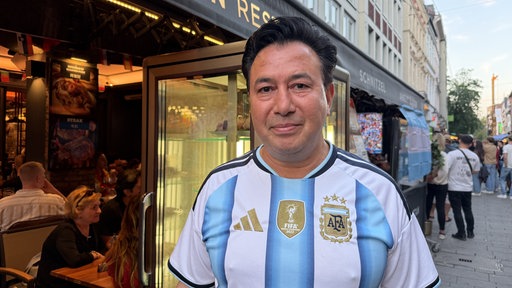 Ein Mann mit himmelblau-weiß-gestreiftem Fußballtrikot steht in der Fußgänger-Zone