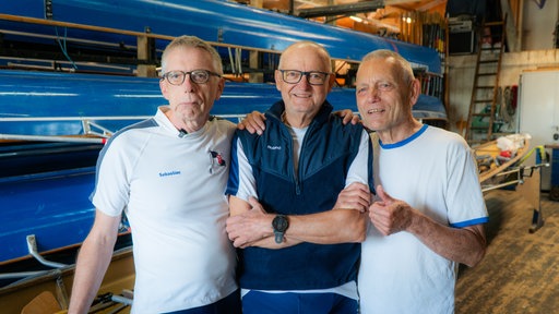Drei Herren stehen im vor ihrem Ruderboot