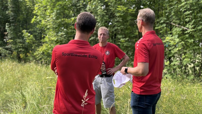 Drei Männer in roten Shirts, auf denen Sportfreunde Echtz steht, stehen auf einer Wiese und unterhalten sich 