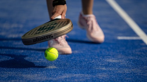 Ein Padelspieler hebt mit dem Schläger einen Ball auf.