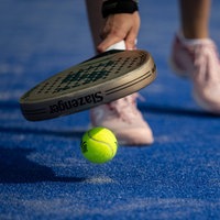 Ein Padelspieler hebt mit dem Schläger einen Ball auf.