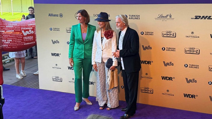 Elena von Spanien mit Hut, weißem Jacket und heller Hose, flankiert von Stefanie Peters und Unternehmer Hermann Bühlbecker.