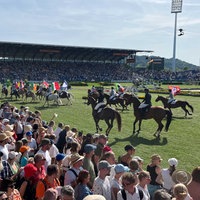 Mehrere Reiter hintereinander, die mit verschiedenen Nationalflaggen über einen Stadion-Rasen reiten.