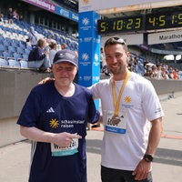 Zwei Männer stehen gemeinsam in einem Marathon-Zieleinlauf und lächeln in die Kamera. Einer von ihnen ist der Ausdauersportler Joey Kelly.