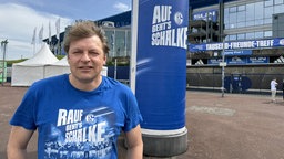 Youri Mulder steht vor der Schalke-Arena. Auf seinem T-Shirt steht "Rauf geht's Schalke".