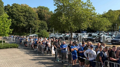 Viele Menschen stehen in einer Schlange, einige in Schalke-Trikots