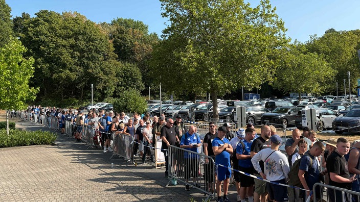 Viele Menschen stehen in einer Schlange, einige in Schalke-Trikots