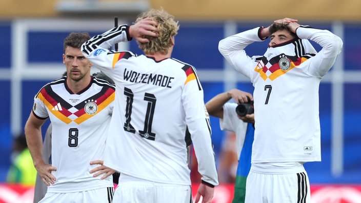 Drei Nationalspieler im Fußballtrikot, Leon Goretzka, Nick Woltemade und Kai Havertz, gucken ernst und traurig