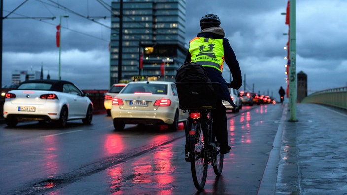 Ein Perosn fährt mit dem Fahrrad über die Deutzer Brücke, auf der Fahrbahn stauen sich diverse Fahrzeuge