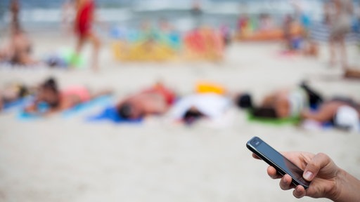 Eine Frau schreibt mit einem Mobiltelefon eine SMS am Strand.