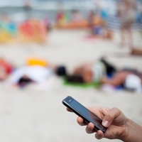 Eine Frau schreibt mit einem Mobiltelefon eine SMS am Strand.