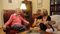 Therapeutin spielt Gitarre, in einem anderen Sessel sitzt eine ältere Frau
