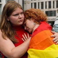 Eine Frau in einer Regenbogenfahne gehüllt lehnt weinend an der Schulter einer weiteren Frau