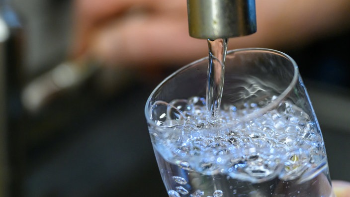 Ein Glas wird unter einem Wasserhahn mit Wasser gefüllt
