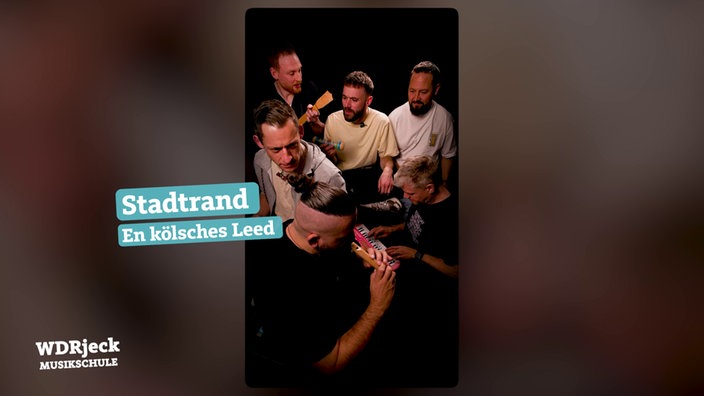 Die Band sitzt in einem engen Studio und spielt auf Kinderinstrumenten