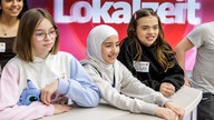 Drei Mädchen lachen vor dem Schriftzug „Lokalzeit“