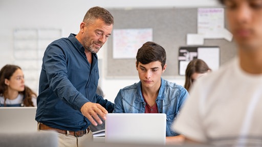Lehrer neben Schüler am Rechner