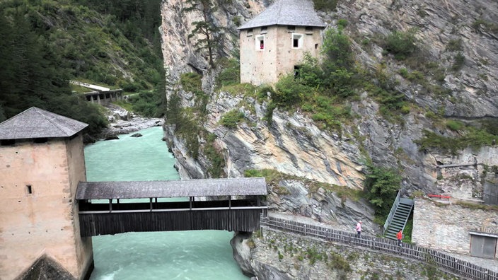 Festungsgebäude an Felswand und eine Brücke über einen Fluss