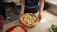 Ein Pizzabäcker präsentiert eine echte neapolitanische Pizza in den Farben weiß, rot und grün