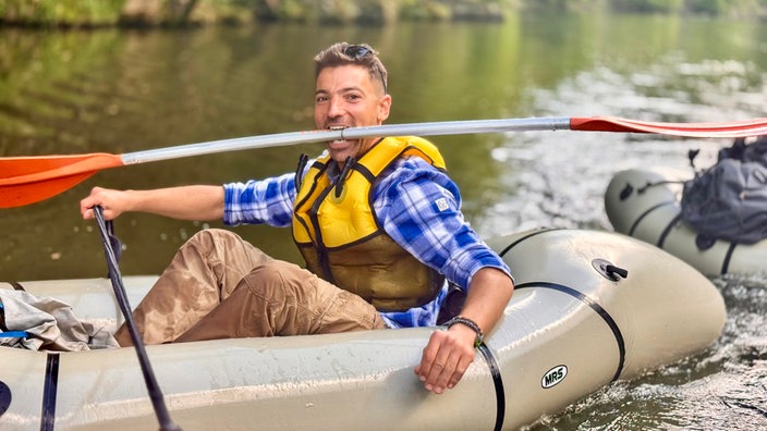 Ramon Babazadeh sitzt in einem Schlauchboot und hält das Paddel mit den Zähnen