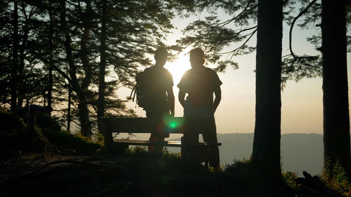 Judith Rakers und ein Wanderer schauen auf eine Waldlandschaft im Sonnenlicht