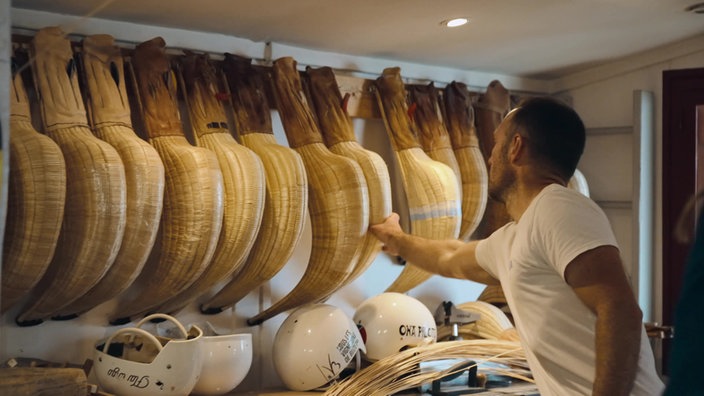 Ein Mann sortiert Pelota-Schläger an einer Wand