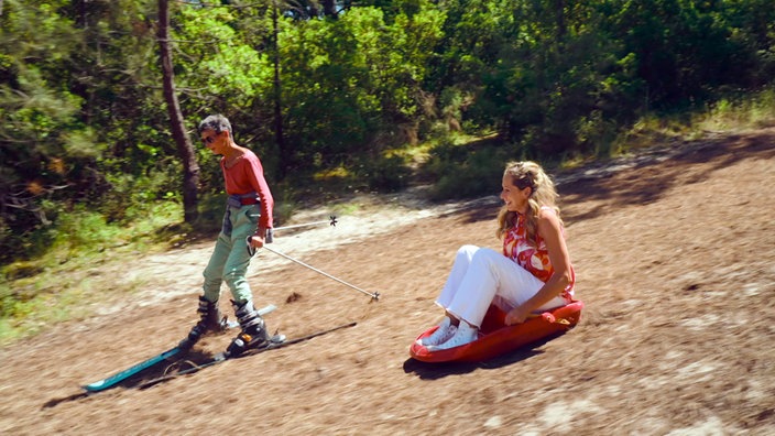 Eine Person auf Skiern und Tamina Kallert auf einem Schlitten am Hang der Düne