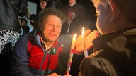 Moderator André Gatzke und ein Kind haben jeweils eine brennende Kerze in der Hand
