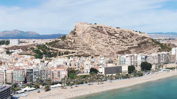 Hochhäuser am Strand, dahinter eine Burg auf einem Berg