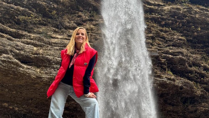 Stephanie Müller-Spirra steht an einem Wasserfall auf einem Felsen.