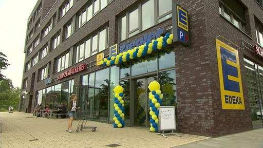 Frau geht mit einem Einkaufswagen in einen Edeka