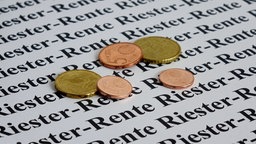 Das Bild zeigt ein paar Cent-Münzen auf einem bedruckten Blatt Papier mit der Aufschruift "Riester-Rente"