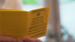 Eine Person hält ein aufgeschlagenes Impfbuch in der Hand