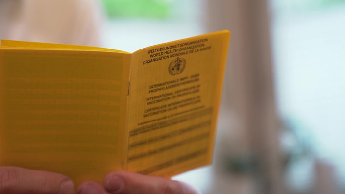Eine Person hält ein aufgeschlagenes Impfbuch in der Hand
