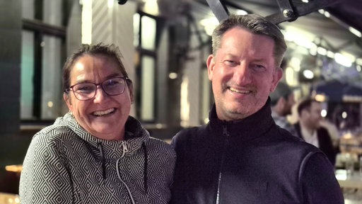 Eine Frau und ihr Partner stehen nebeneinander auf der Außenterrasse einer Kneipe in der Düsseldorfer Altstadt.