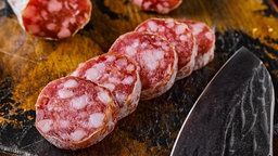 Symbolbild fermentierte Salamiwürste auf Holzschneidebrett in Scheiben geschnitten, kann von getesteten Salamis abweichen. 